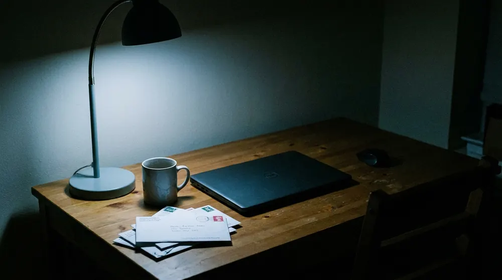 Un escritorio vacío de noche, con el portátil cerrado, una taza fría y correo sin abrir